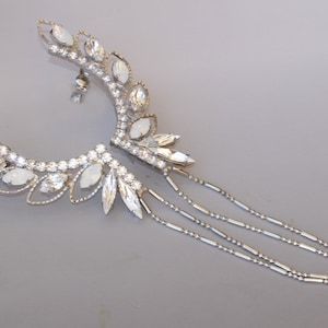 May include: A silver ear cuff with a delicate design featuring white crystal accents and a dangling chain.
