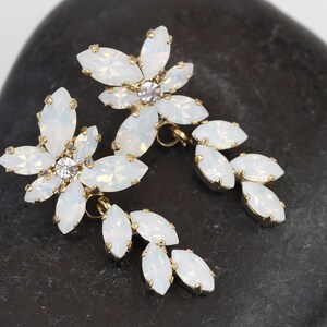 May include: A pair of white opal flower earrings with gold accents. The earrings feature a cluster of marquise-shaped stones in a flower design, with a smaller cluster of stones dangling below.