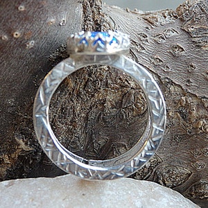 May include: A silver ring featuring a blue gemstone set in a silver bezel. The ring band is textured with a repeating pattern.