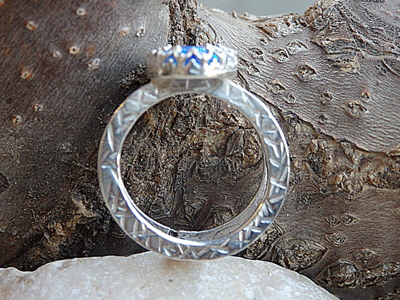 May include: A silver ring featuring a blue gemstone set in a silver bezel. The ring band is textured with a repeating pattern.