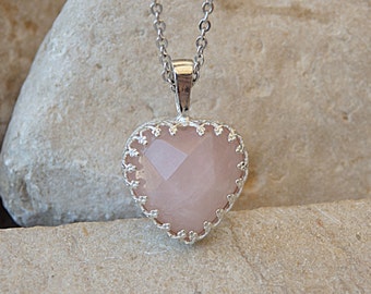 May include: A silver heart-shaped pendant with a pink rose quartz stone. The pendant is on a silver chain.