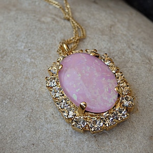 Pu&ograve; includere: Una collana d'oro con una pietra ovale rosa circondata da strass trasparenti.