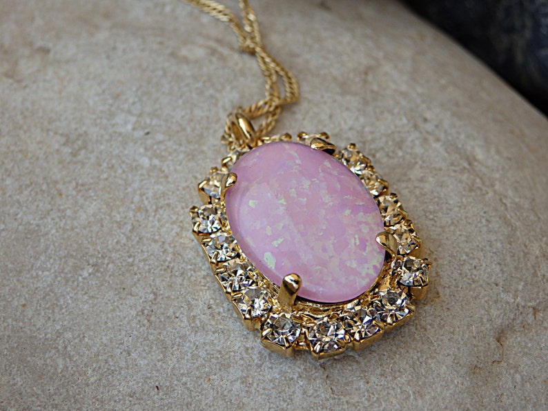 Pu&ograve; includere: Una collana d'oro con una pietra ovale rosa circondata da strass trasparenti.