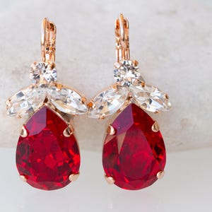 May include: A pair of dangle earrings with a teardrop-shaped red gemstone and a cluster of clear rhinestones.