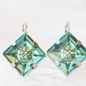 Può includere: Un paio di orecchini d'argento con cristalli quadrati sfaccettati di colore verde acqua. I cristalli hanno un leggero bagliore iridescente.