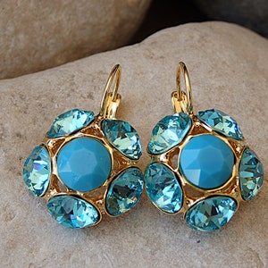 Puede incluir: Un par de pendientes colgantes de oro con una piedra central azul turquesa rodeada de piedras m&aacute;s peque&ntilde;as de color azul turquesa.