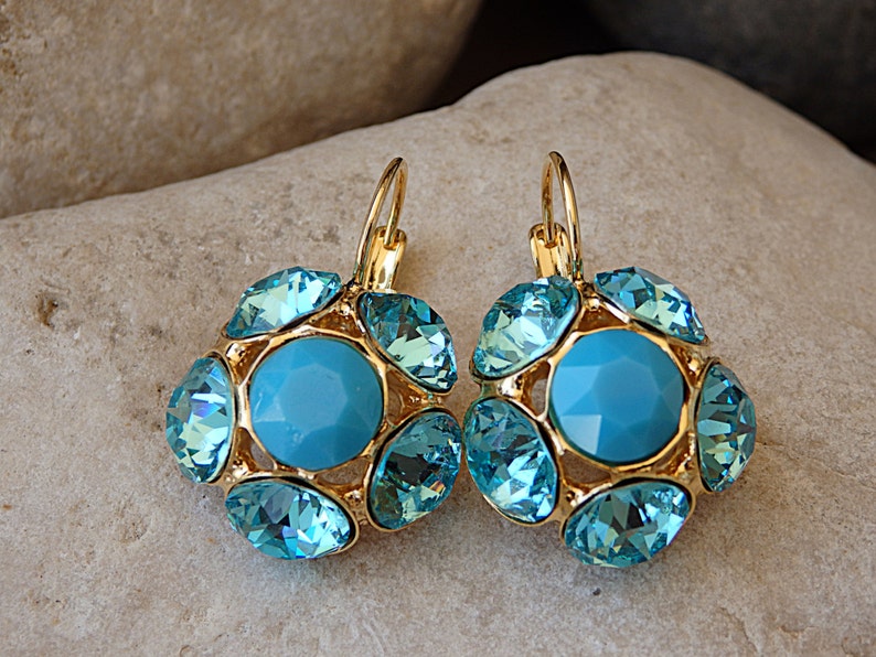 Puede incluir: Un par de pendientes colgantes de oro con una piedra central azul turquesa rodeada de piedras m&aacute;s peque&ntilde;as de color azul turquesa.