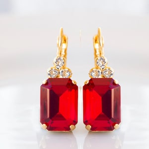 May include: A pair of gold earrings with red gemstone drops and clear crystal accents.
