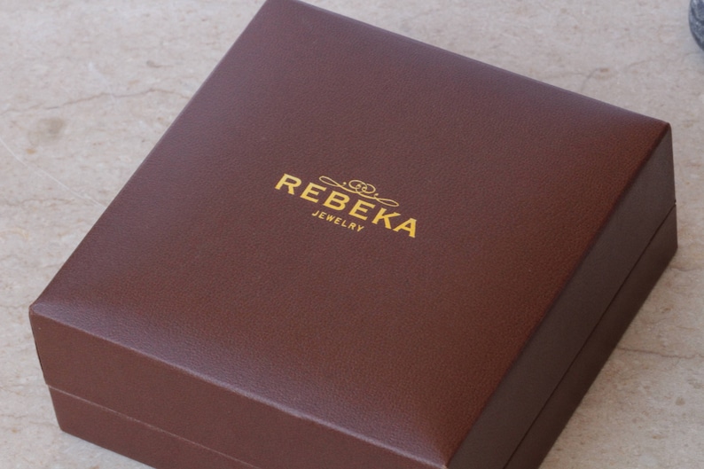 May include: A brown rectangular box with the text "REBEKA JEWELRY" in gold lettering.