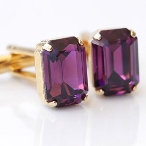 Könnte beinhalten: Ein Paar goldene Manschettenknöpfe mit rechteckigen violetten Edelsteinen.
