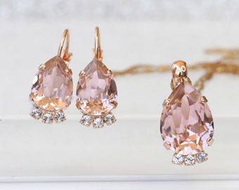 Puede incluir: Un conjunto de joyas de oro rosa con un colgante en forma de lágrima y pendientes a juego. El colgante y los pendientes están adornados con cristales transparentes.