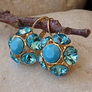 Puede incluir: Un par de pendientes de oro con piedras de cristal azul. Los pendientes tienen forma de racimo de piedras redondas.