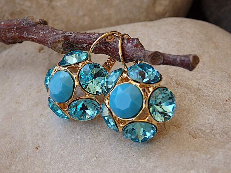 Puede incluir: Un par de pendientes de oro con piedras de cristal azul. Los pendientes tienen forma de racimo de piedras redondas.