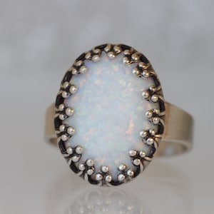 May include: A silver ring with a white opal stone set in a decorative silver bezel. The bezel has a scalloped edge with small silver beads.