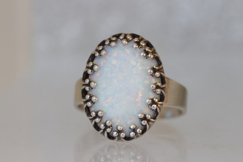 May include: A silver ring with a white opal stone set in a decorative silver bezel. The bezel has a scalloped edge with small silver beads.