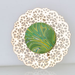 May include: A green and yellow marbled circle brooch with a gold filigree design.
