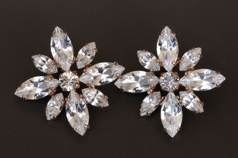 May include: A pair of gold tone earrings with clear crystal marquise shaped stones arranged in a flower design.