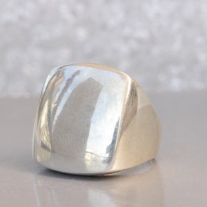 May include: A silver ring with a smooth, square-shaped top.