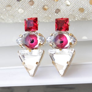 May include: A pair of earrings with a red square, a clear eye-shaped stone with a red center, and a clear triangular stone.