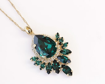 May include: A gold chain necklace with a large emerald green pear-shaped pendant surrounded by smaller emerald green and clear rhinestones.