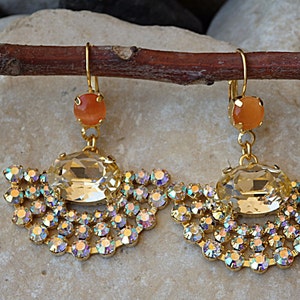 May include: A pair of gold earrings with a large clear crystal and a smaller orange stone. The earrings are decorated with a fringe of smaller crystals.