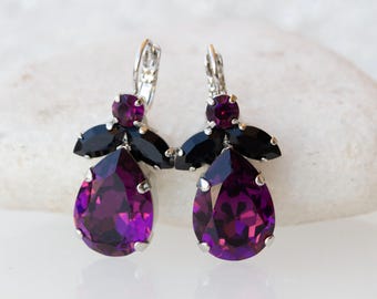 May include: A pair of dangle earrings with a teardrop-shaped purple crystal and black accents.