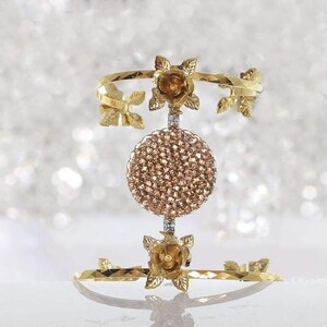 May include: Gold-tone bracelet with a circular design featuring pink rhinestones. The bracelet has a floral design with leaves and roses.