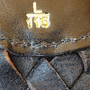 May include: Close-up of a black leather strap with a gold embossed label that reads "L 115".