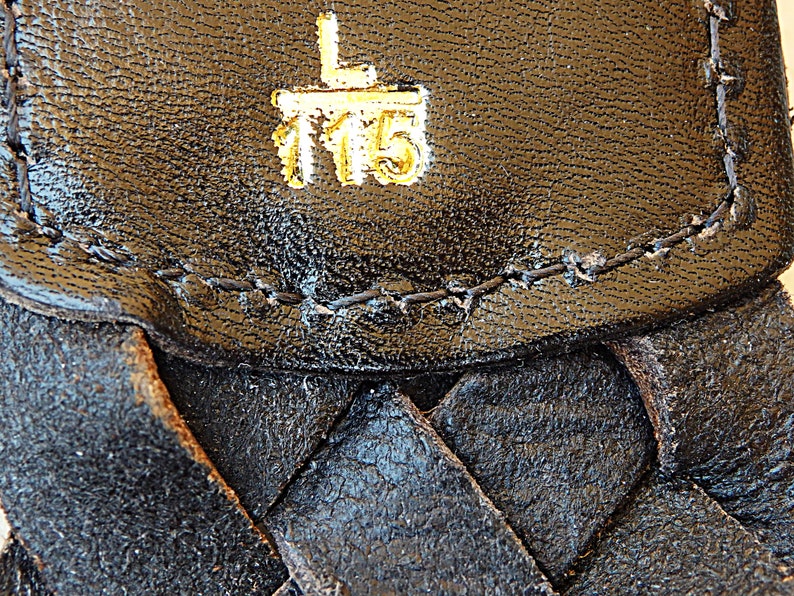 May include: Close-up of a black leather strap with a gold embossed label that reads "L 115".