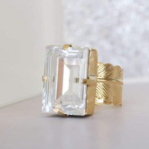 May include: A gold ring with a large, clear, rectangular gemstone and a feather-shaped band.