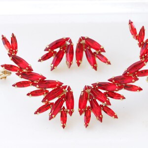 May include: A pair of red crystal ear climbers with gold-tone settings. The earrings are designed in a leaf shape and have a clip-on closure.