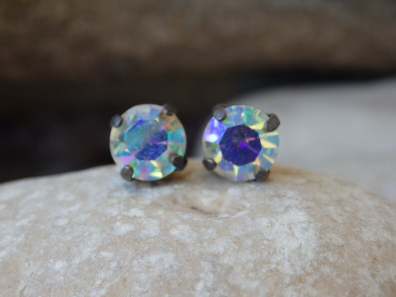 May include: A pair of iridescent silver stud earrings with a round, faceted crystal.