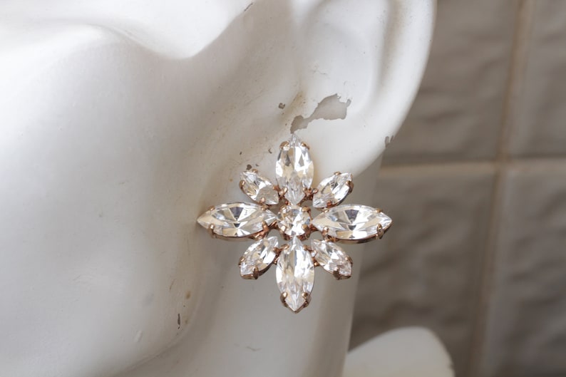 May include: A pair of gold tone earrings with a large, clear crystal flower design.