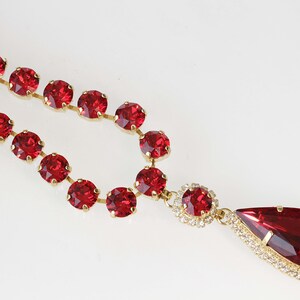 May include: A red rhinestone necklace with a teardrop pendant. The necklace is made of small round rhinestones and the pendant is surrounded by smaller rhinestones.