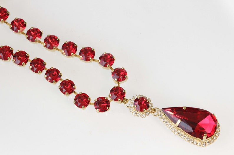 May include: A red rhinestone necklace with a teardrop pendant. The necklace is made of small round rhinestones and the pendant is surrounded by smaller rhinestones.