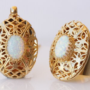 Puede incluir: Un par de anillos de tono dorado con una piedra de ópalo engastada en un diseño de filigrana. Los anillos son de forma ovalada y tienen un patrón delicado e intrincado.