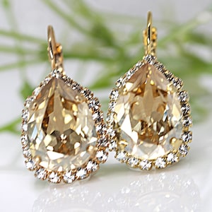 May include: A pair of gold-toned drop earrings. Each earring features a large, pear-shaped, champagne-colored crystal surrounded by a halo of smaller, clear crystals. The earrings have a lever-back closure.