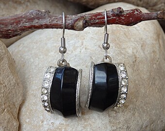 May include: A pair of black and silver earrings with a row of clear rhinestones around the edge of each earring.