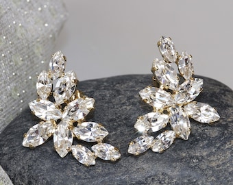 May include: A pair of gold earrings with clear crystal marquise-shaped stones arranged in a floral design.