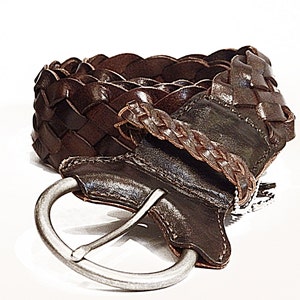 May include: A brown leather braided belt with a silver buckle. The belt is woven in a basket weave pattern.