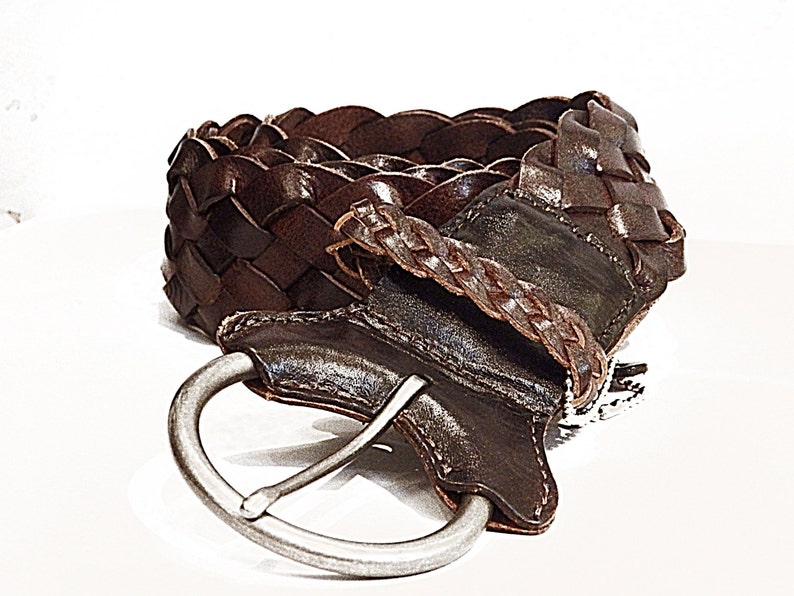 May include: A brown leather braided belt with a silver buckle. The belt is woven in a basket weave pattern.