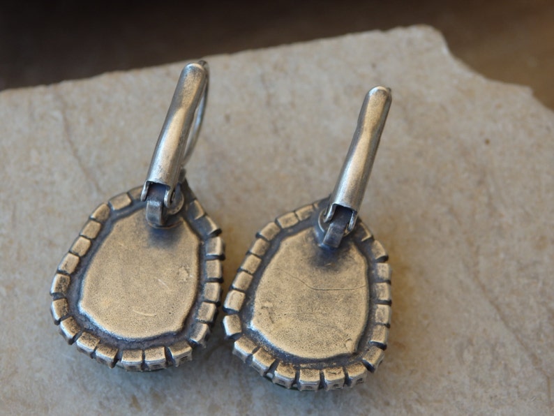May include: A pair of silver earrings with a teardrop-shaped design. The earrings have a textured edge and a silver hook closure.