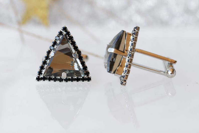 Puede incluir: Un par de gemelos de plata con detalles de cristal negro. Un gemelo tiene forma triangular, el otro tiene forma cuadrada.