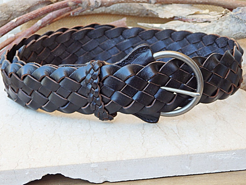 May include: A dark brown leather belt with a braided design and a silver buckle.