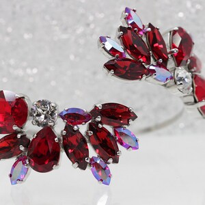 May include: A silver cuff bracelet with red and iridescent crystal accents. The bracelet is open on one side and has a curved shape.