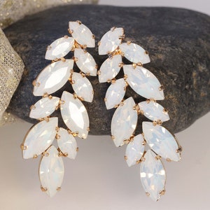May include: A pair of long, white, teardrop-shaped crystal earrings with a gold setting. The earrings are arranged in a cascading pattern.