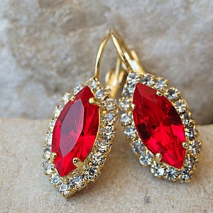 Puede incluir: Un par de pendientes de oro con una gran piedra roja en forma de marquesa rodeada de piedras más pequeñas y transparentes.