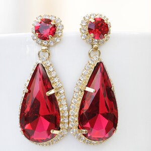 May include: A pair of gold tone dangle earrings with teardrop shaped red crystal stones and smaller round red crystal stones at the top.