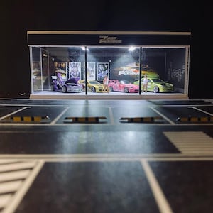 May include: A miniature diorama featuring several colorful model cars displayed inside a glass case. The cars are various colors, including purple, yellow, pink, and green. The case has a black roof with the text "The Fast and the Furious".