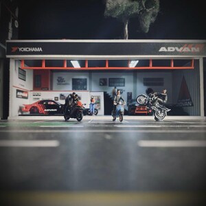May include: Miniature diorama of a garage with the Yokohama and Advan logos. Several small motorcycles and a car are in front of the garage. One motorcycle is doing a wheelie. Several miniature people are in the scene.